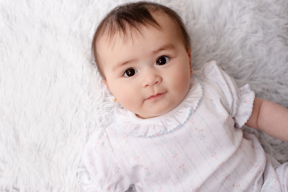 Bebê de body branco com babadinho deitada em manta felpuda passalinho